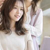 美容院レビューの例文を紹介する記事のアイキャッチ画像。ヘアサロンで仕上がりを確認する女性とレビュー入力をイメージした場面