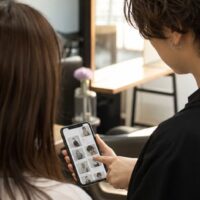 ヘアサロンの集客方法と動線設計を示す、スマートフォンで予約ページを確認する美容師