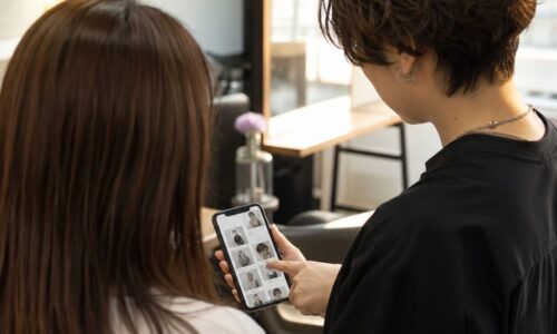 ヘアサロンの集客方法と動線設計を示す、スマートフォンで予約ページを確認する美容師