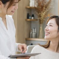 サロンで丁寧な接客をするスタッフと笑顔のお客様。サロンの高評価口コミを増やす小さな気配りを表現したイメージ
